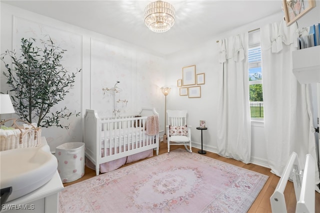 bedroom with baseboards, a crib, a notable chandelier, and wood finished floors