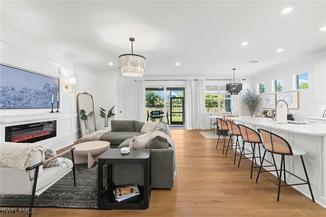 living room with a chandelier, a glass covered fireplace, recessed lighting, and light wood-style floors