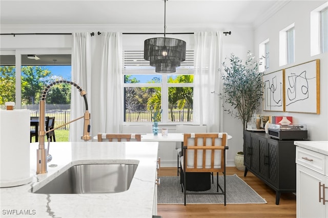 kitchen with light stone countertops, ornamental molding, a sink, light wood-style floors, and white cabinetry