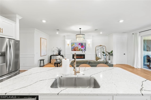 kitchen with a sink, stainless steel refrigerator with ice dispenser, a glass covered fireplace, crown molding, and open floor plan