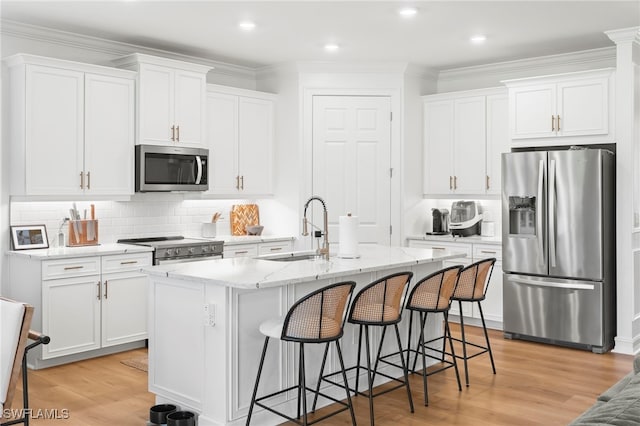 kitchen featuring a center island with sink, light wood-style flooring, a sink, white cabinetry, and stainless steel appliances