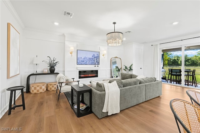 living area with a glass covered fireplace, an inviting chandelier, wood finished floors, and crown molding