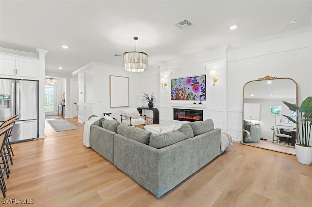 living area featuring visible vents, light wood finished floors, an inviting chandelier, ornamental molding, and a glass covered fireplace