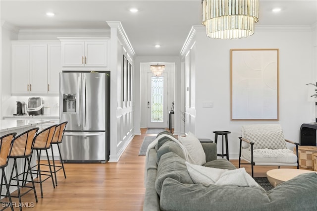 living area with a chandelier, light wood-style flooring, and ornamental molding