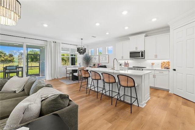 kitchen with a sink, decorative backsplash, white cabinets, stainless steel microwave, and open floor plan