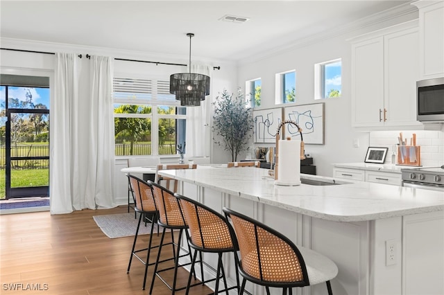 kitchen featuring stainless steel microwave, visible vents, ornamental molding, light wood-style floors, and white cabinetry