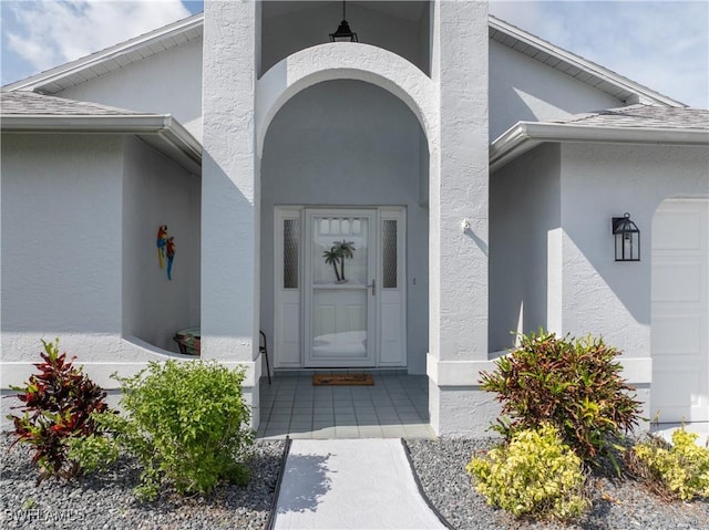 entrance to property with a garage, a shingled roof, and stucco siding