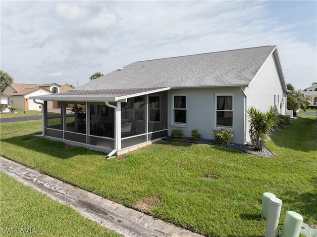 back of house featuring a sunroom, roof with shingles, a yard, and stucco siding