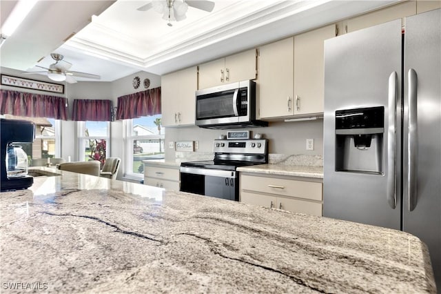 kitchen with ceiling fan, light stone counters, cream cabinets, stainless steel appliances, and crown molding