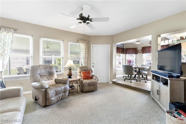 living area with light carpet, a ceiling fan, and baseboards