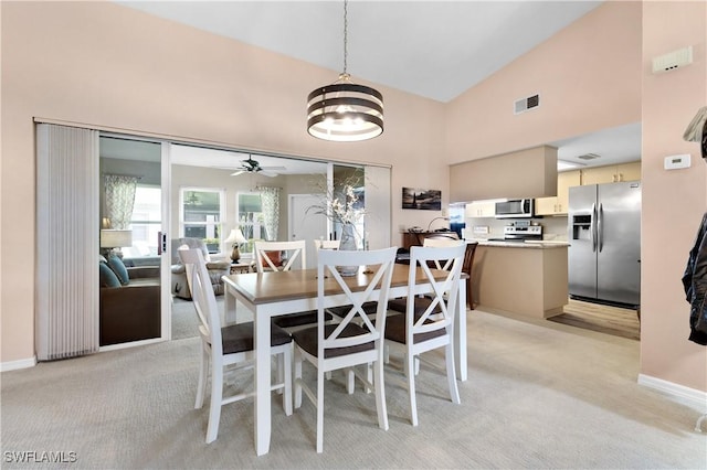 dining area featuring light colored carpet, visible vents, a ceiling fan, high vaulted ceiling, and baseboards