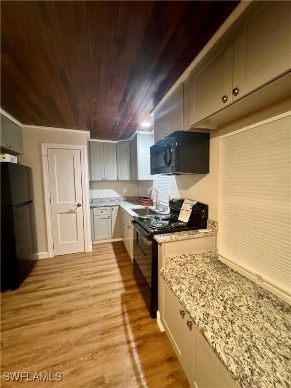 kitchen featuring wood ceiling, a sink, light stone countertops, light wood-type flooring, and black appliances