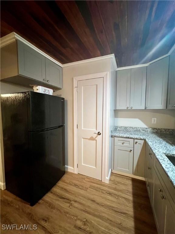 kitchen featuring light stone countertops, wooden ceiling, wood finished floors, and freestanding refrigerator