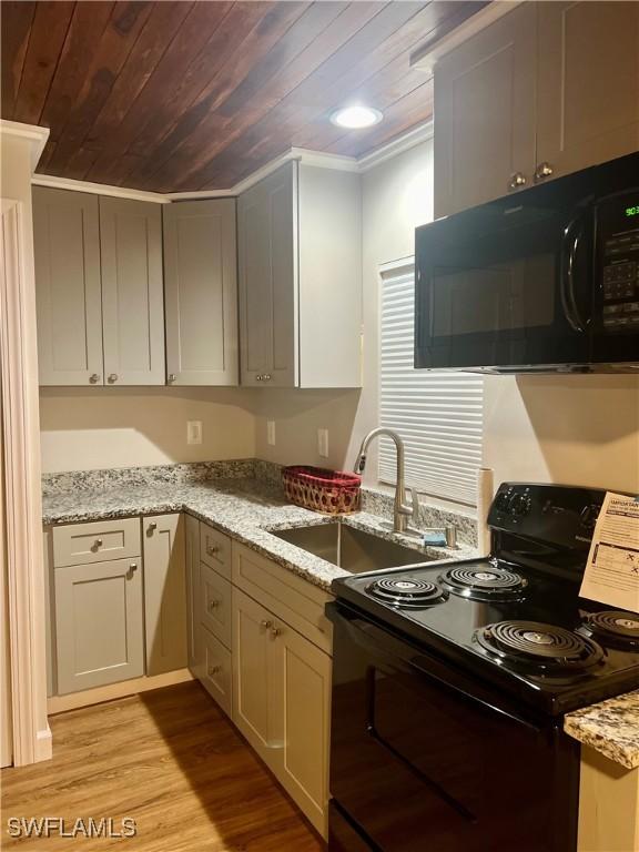 kitchen featuring light wood-style floors, wood ceiling, light stone counters, black appliances, and a sink