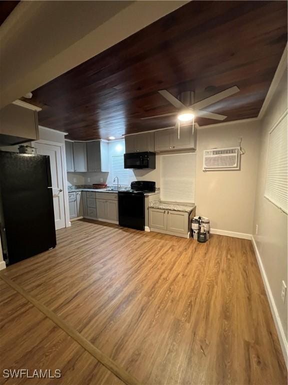 kitchen with light countertops, light wood-style floors, black appliances, a wall mounted air conditioner, and baseboards