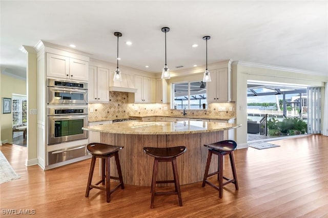 kitchen featuring crown molding, a warming drawer, double oven, a healthy amount of sunlight, and a kitchen island