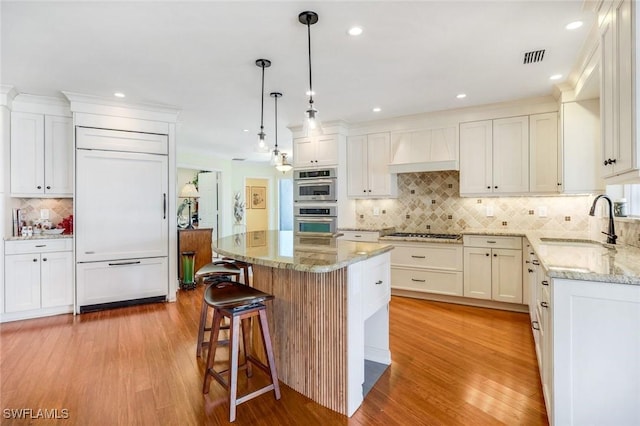 kitchen with light wood-type flooring, premium range hood, paneled built in refrigerator, and a sink