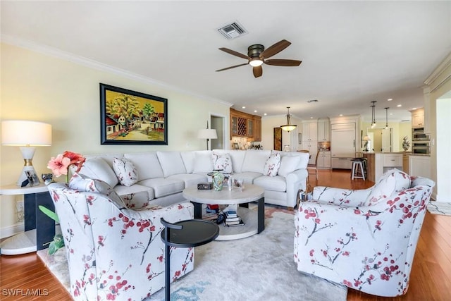 living room with visible vents, crown molding, light wood-style flooring, and ceiling fan