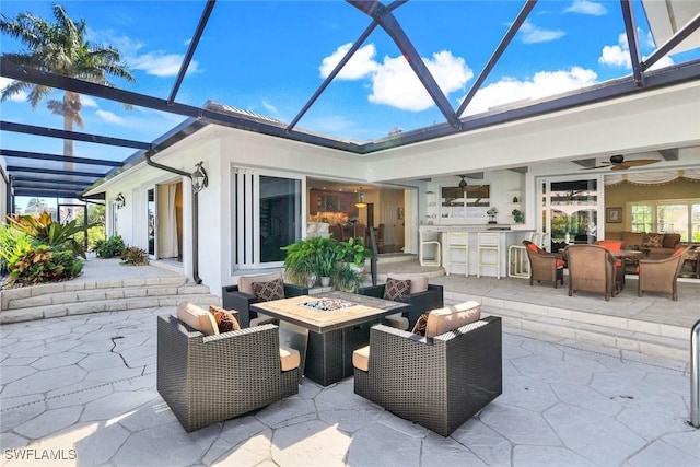 view of patio / terrace with a lanai, an outdoor living space with a fire pit, ceiling fan, and outdoor dry bar