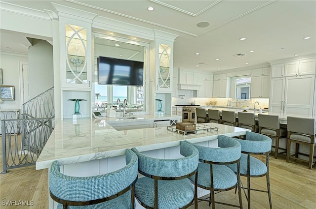 kitchen with crown molding, a breakfast bar area, light wood-style floors, white cabinets, and a peninsula