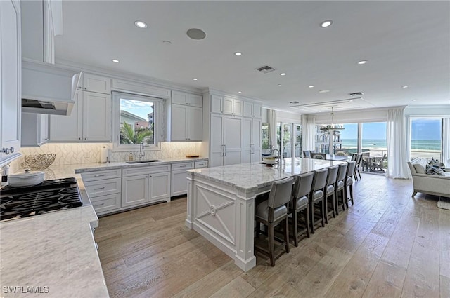 kitchen with a large island, tasteful backsplash, visible vents, light wood-style flooring, and a sink