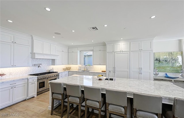 kitchen featuring range with two ovens, visible vents, backsplash, white cabinetry, and a sink