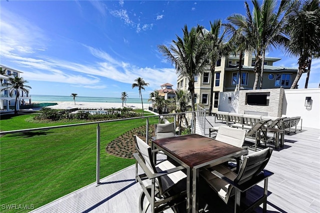 wooden terrace featuring outdoor dining space, a lawn, a water view, and a fireplace