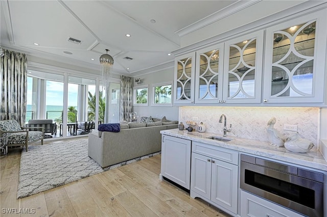 kitchen with light stone counters, stainless steel microwave, visible vents, ornamental molding, and a sink