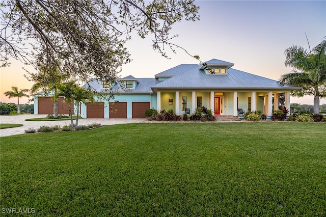 view of front of house featuring driveway, a garage, a lawn, metal roof, and a porch