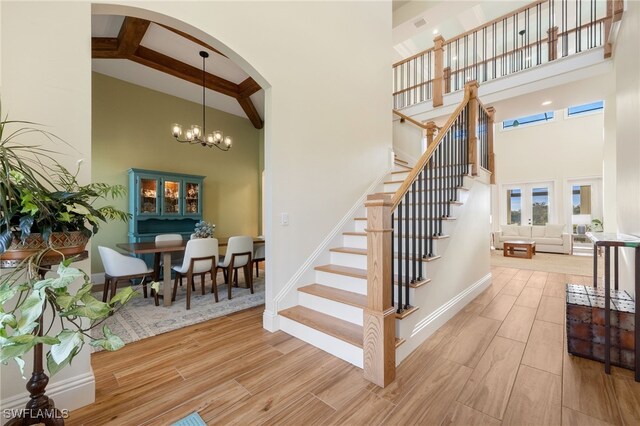 stairway with a towering ceiling, an inviting chandelier, and wood finished floors