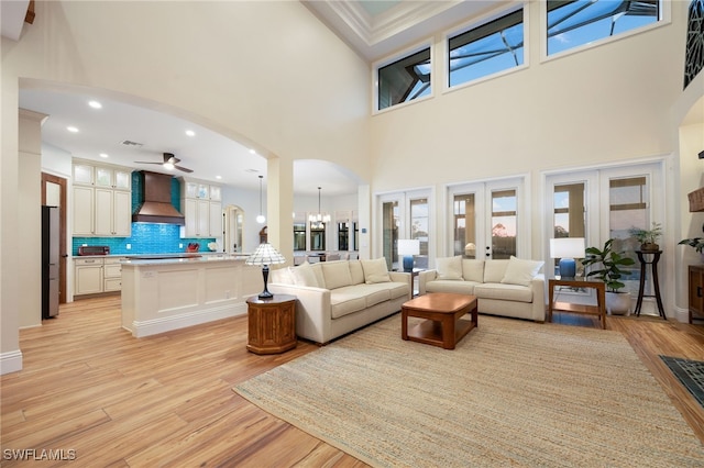 living room with arched walkways, light wood-style flooring, recessed lighting, ceiling fan with notable chandelier, and french doors