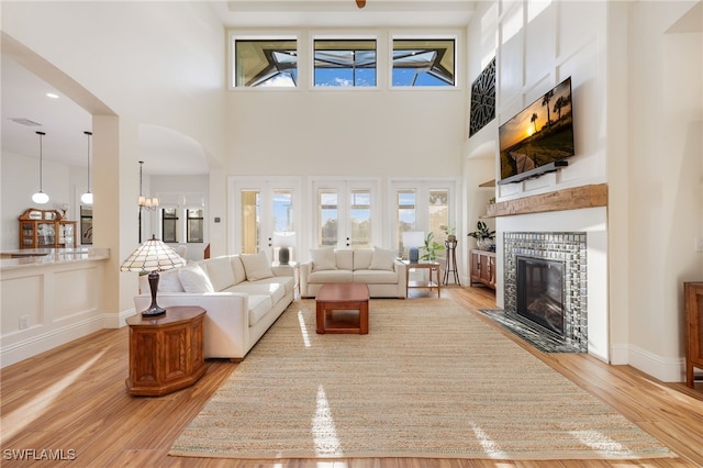 living room with arched walkways, a fireplace, light wood-style flooring, and a high ceiling