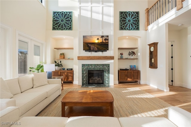 living room with baseboards, a high ceiling, light wood-type flooring, built in shelves, and a fireplace