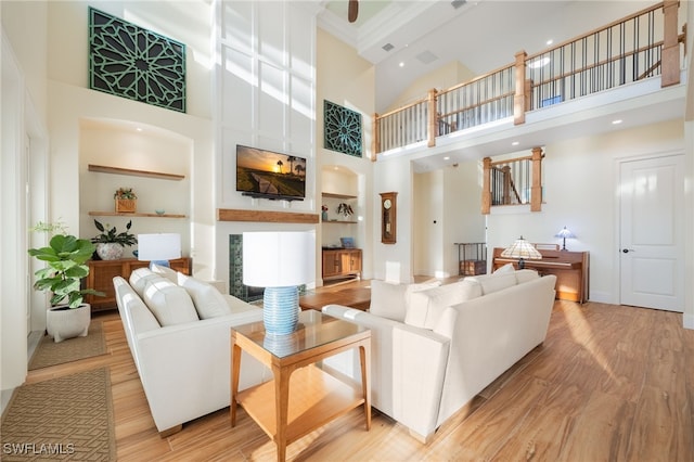 living area with built in shelves, light wood-type flooring, a fireplace, and a towering ceiling