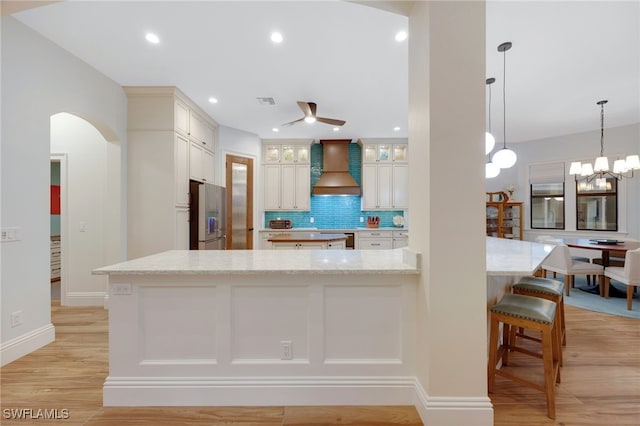 kitchen with arched walkways, premium range hood, stainless steel refrigerator with ice dispenser, light wood finished floors, and tasteful backsplash