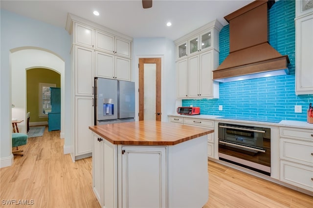 kitchen featuring arched walkways, electric stovetop, premium range hood, butcher block countertops, and refrigerator with ice dispenser