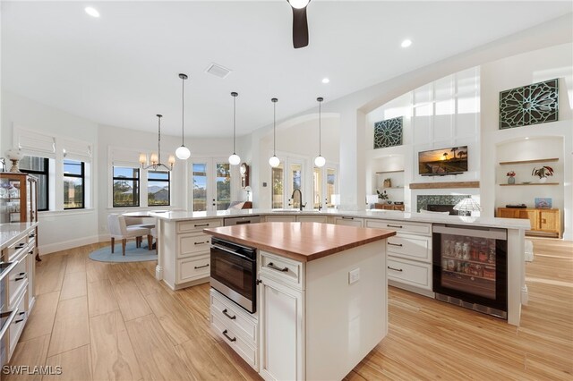 kitchen featuring beverage cooler, a large island with sink, light wood-type flooring, built in shelves, and wooden counters