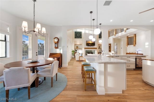 kitchen featuring beverage cooler, visible vents, white cabinets, light wood-style flooring, and a fireplace