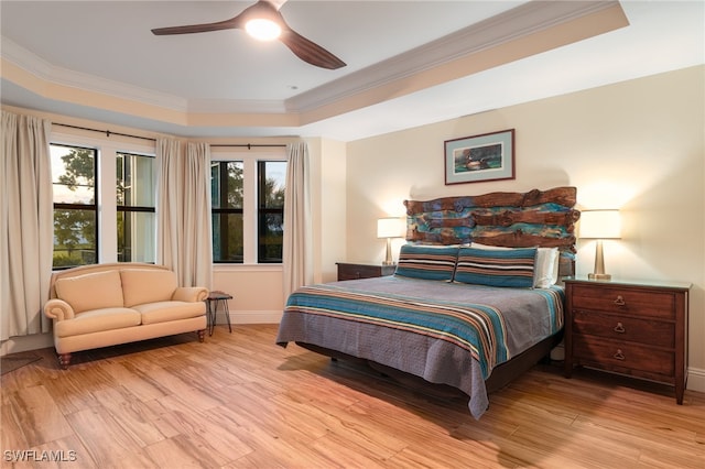 bedroom with baseboards, a tray ceiling, light wood-type flooring, and crown molding