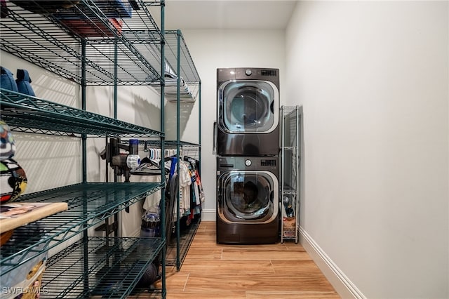 laundry room with laundry area, stacked washing maching and dryer, wood finished floors, and baseboards