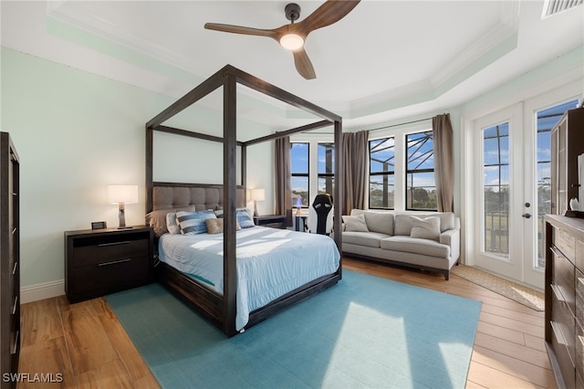 bedroom with visible vents, wood finished floors, access to exterior, a tray ceiling, and french doors