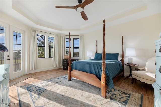 bedroom featuring access to outside, a tray ceiling, wood finished floors, and crown molding