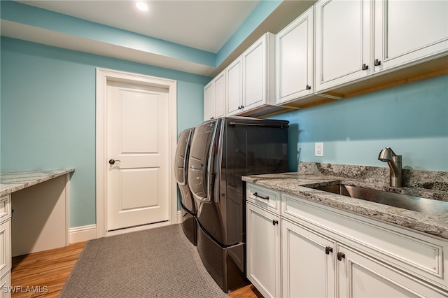 laundry area with washing machine and clothes dryer, cabinet space, light wood-style flooring, a sink, and baseboards