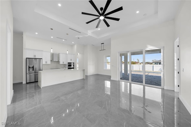 unfurnished living room with ceiling fan, marble finish floor, a high ceiling, and a raised ceiling