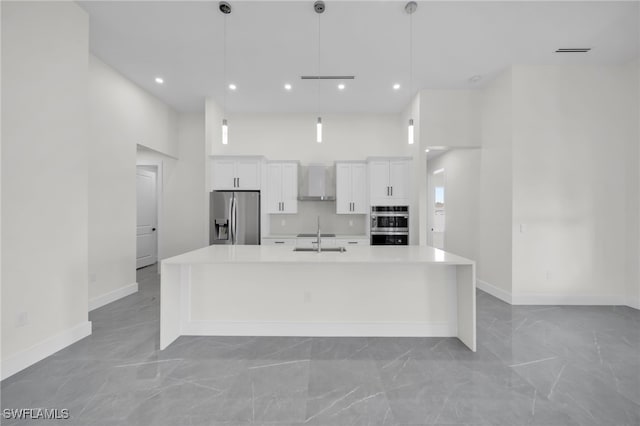 kitchen featuring a spacious island, a towering ceiling, appliances with stainless steel finishes, white cabinets, and wall chimney exhaust hood