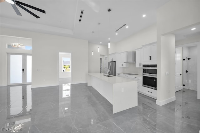 kitchen with stainless steel appliances, a high ceiling, white cabinetry, marble finish floor, and wall chimney exhaust hood