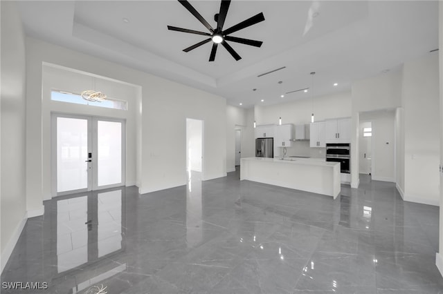 unfurnished living room with a high ceiling, a sink, marble finish floor, french doors, and a tray ceiling