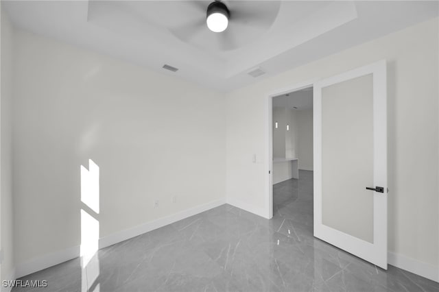 empty room featuring marble finish floor, a tray ceiling, visible vents, and baseboards