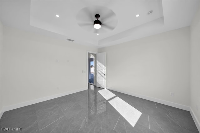 empty room featuring visible vents, a tray ceiling, ceiling fan, and baseboards