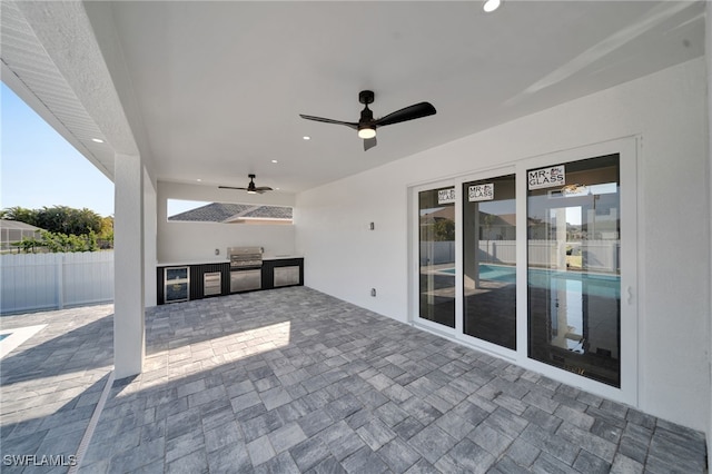 view of patio / terrace with beverage cooler, a ceiling fan, area for grilling, fence, and exterior kitchen